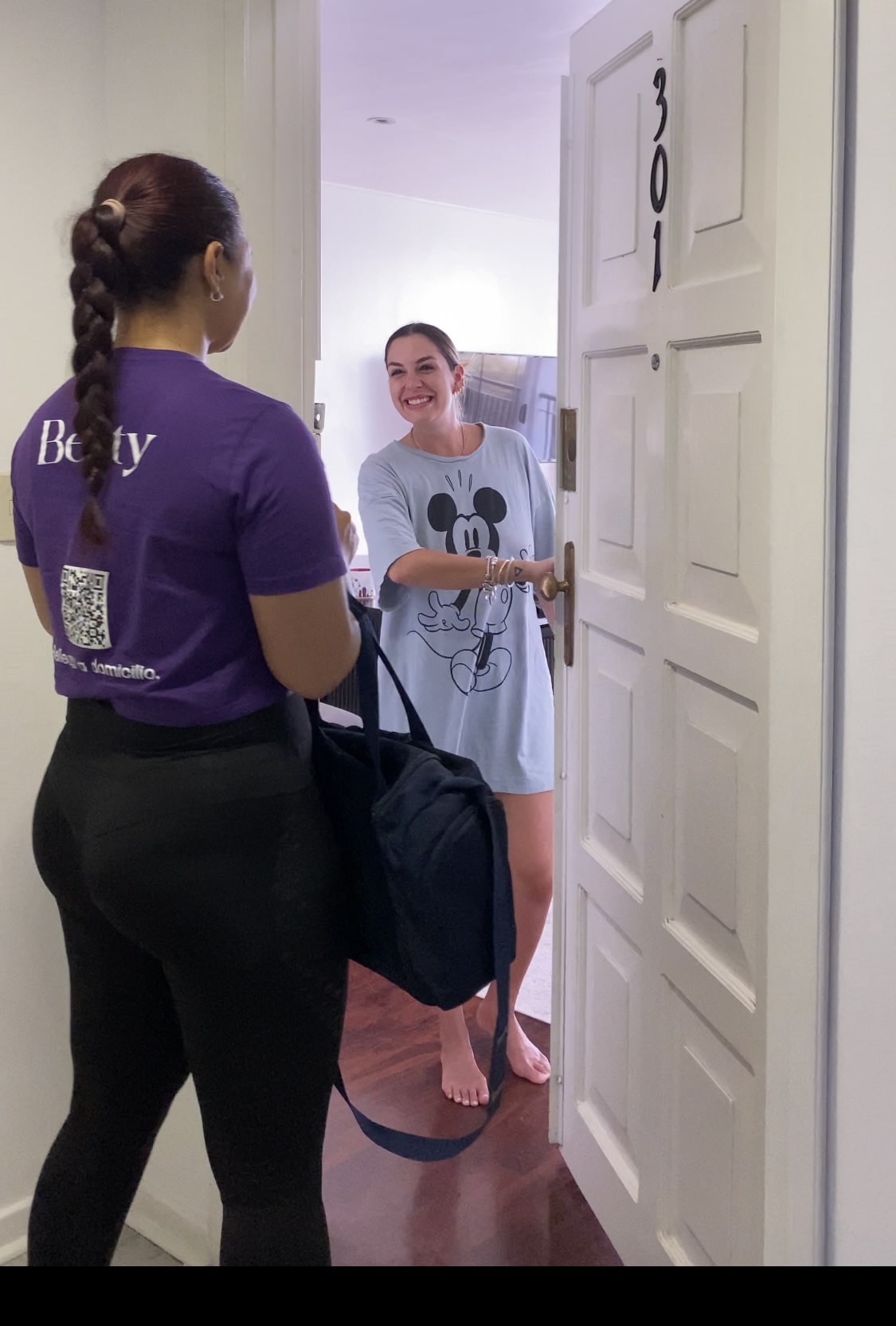 Especialista de Belity atendiendo a una clienta que le abre la puerta de su casa para un servicio de belleza a domicilio